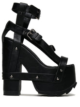 Load image into Gallery viewer, outer view of black vegan leather strappy platform sandal with 6.5" heel. Sandal has gunmetal hardware, adjustable ankle strap and adjustable side strap. Bottom of front platform has a fanned grip for better stability.