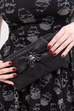 Load image into Gallery viewer, Black clutch with spider embellishment held by a person wearing a black dress with skull pattern.
