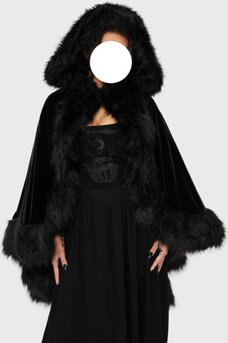 Model wearing a black faux fur-trimmed hooded cloak over a black dress on a white background