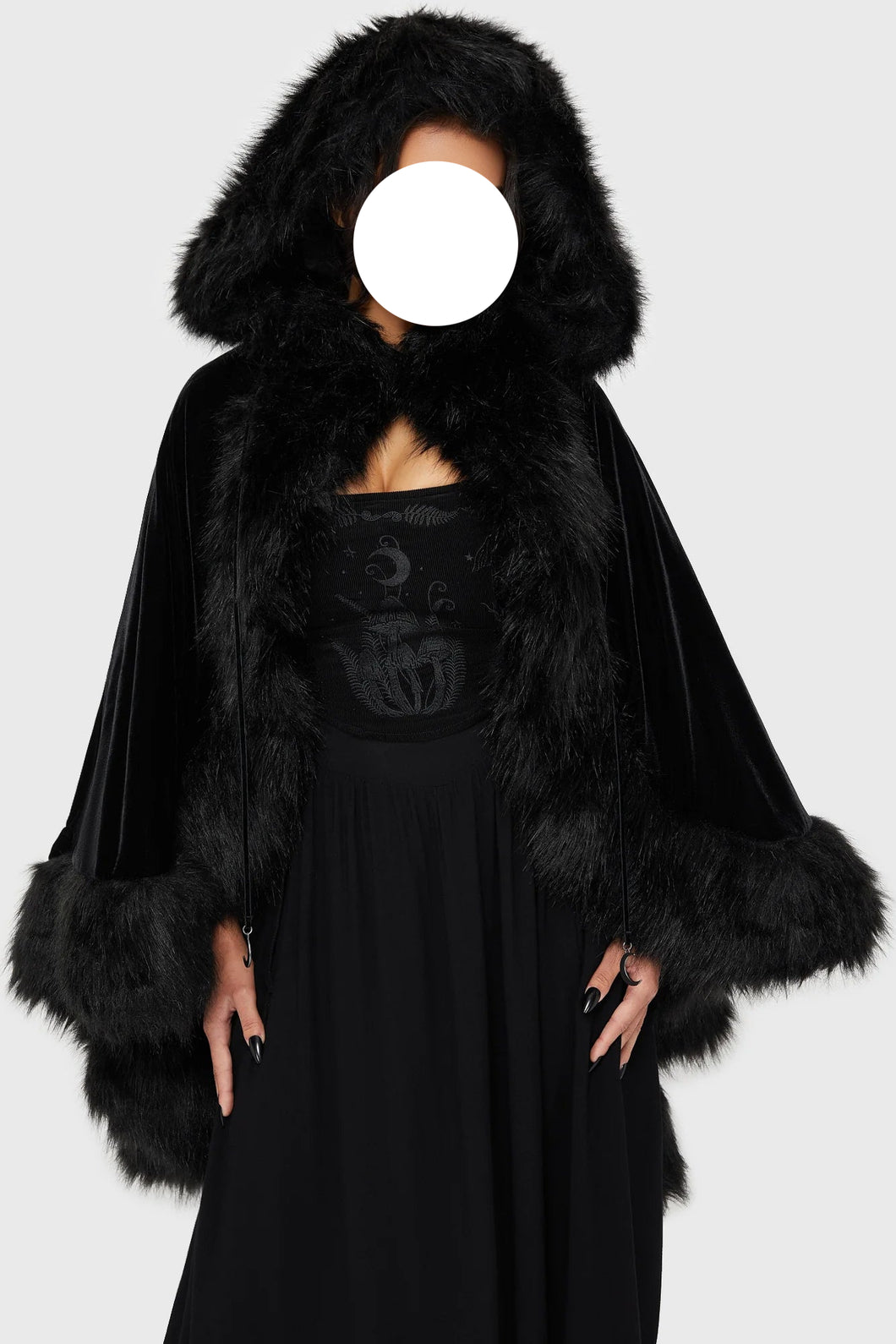 Model wearing a black faux fur-trimmed hooded cloak over a black dress on a white background