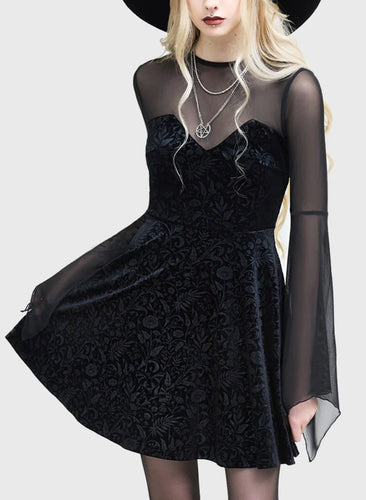 Model wearing a black dress with sheer sleeves and a black hat on a white background
