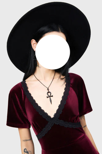 Person wearing a black hat and burgundy velvet dress with a black collar against a white background