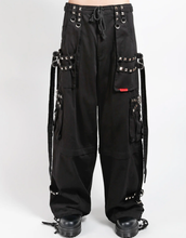 Load image into Gallery viewer, Waist-down view of baggy black punk-style cargo pants featuring silver pyramid studs, hanging side straps, a drawstring waist, and chunky black boots against a white background.
