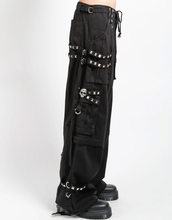 Load image into Gallery viewer, Waist-down view of baggy black punk-style cargo pants featuring silver pyramid studs, hanging side straps, a drawstring waist, and chunky black boots against a white background.

