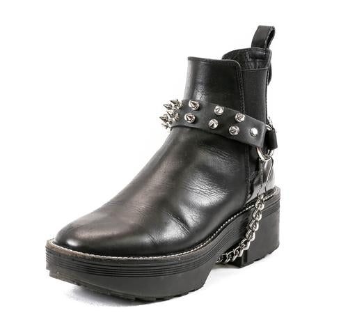 black ankle boot displaying black leather boot strap with two rows of silver tree spikes, single silver o ring and silver hanging chain