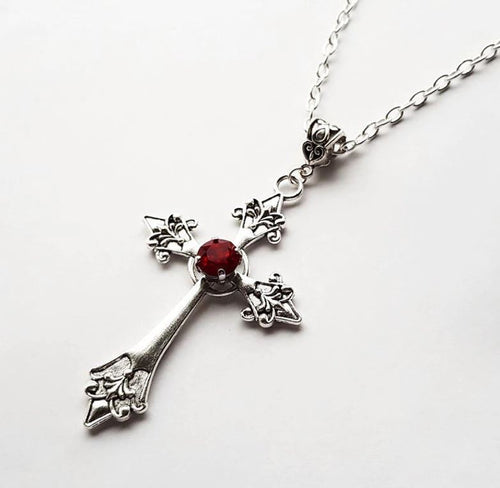 Silver colored zinc alloy vampire cross necklace with red cubic zirconia gem in center of cross.