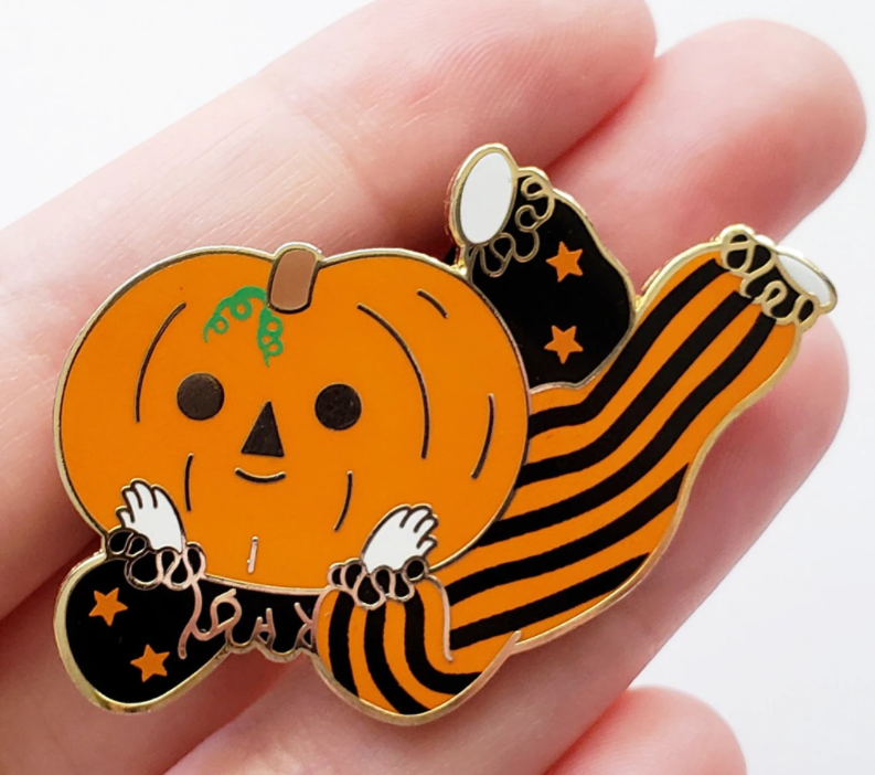 Orange pumpkin head boy with cute clown costume on. One side of his costume is black and orange striped, and the other half is black with orange stars.