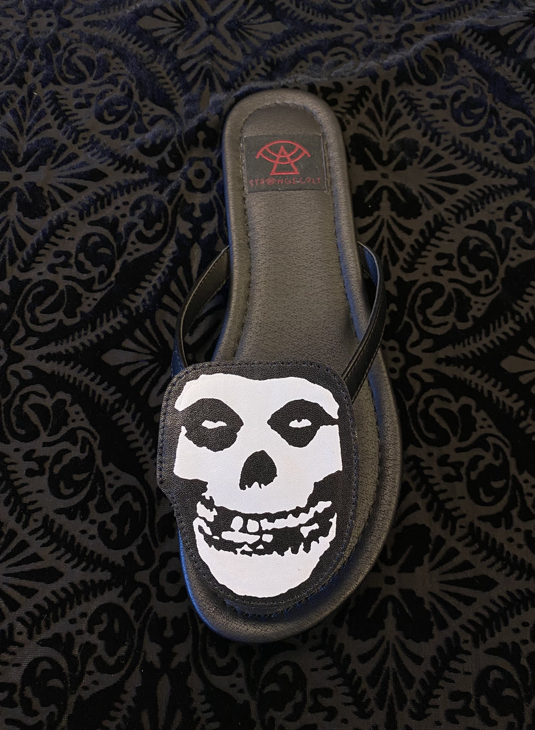 top of Black flat sandal with vegan leather Misfits fiend skull cutout on top. Vegan leather with black rubber outsole.