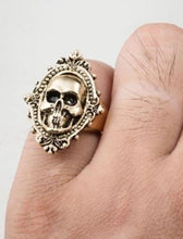 Load image into Gallery viewer, Gold colored zinc alloy skull ring with pretty oval detailed frame around skull.
